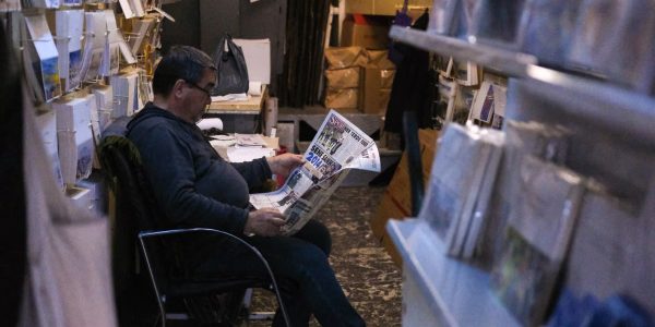 Gentleman sits comfortably reading a newspaper in a cozy, dimly lit bookstore.