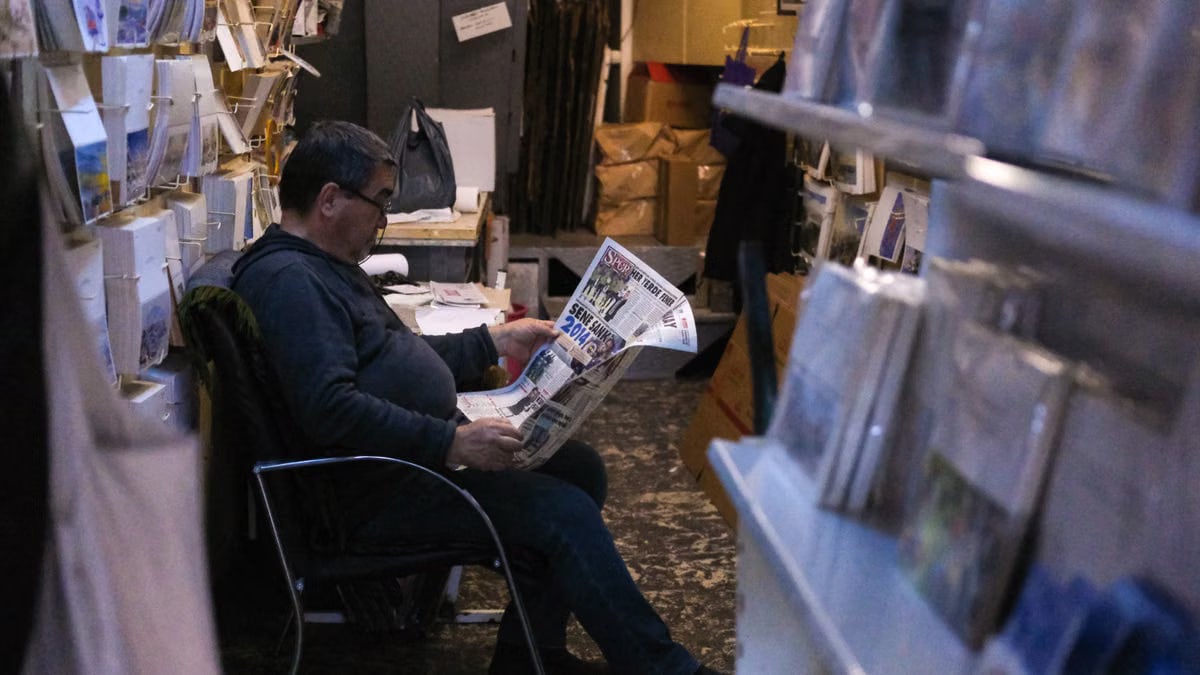 Gentleman sits comfortably reading a newspaper in a cozy, dimly lit bookstore.